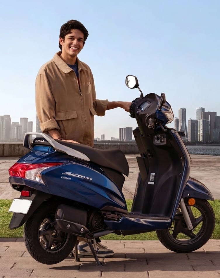 a boy standing with smile side honda activa average per liter